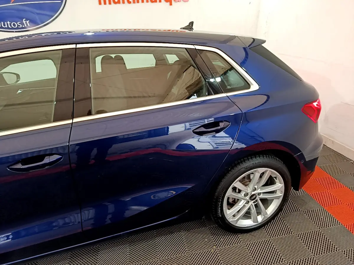 Profil côté droit d'une Audi A3 bleu 2023 avec jantes alliage et feux arrière LED visibles en intérieur showroom.