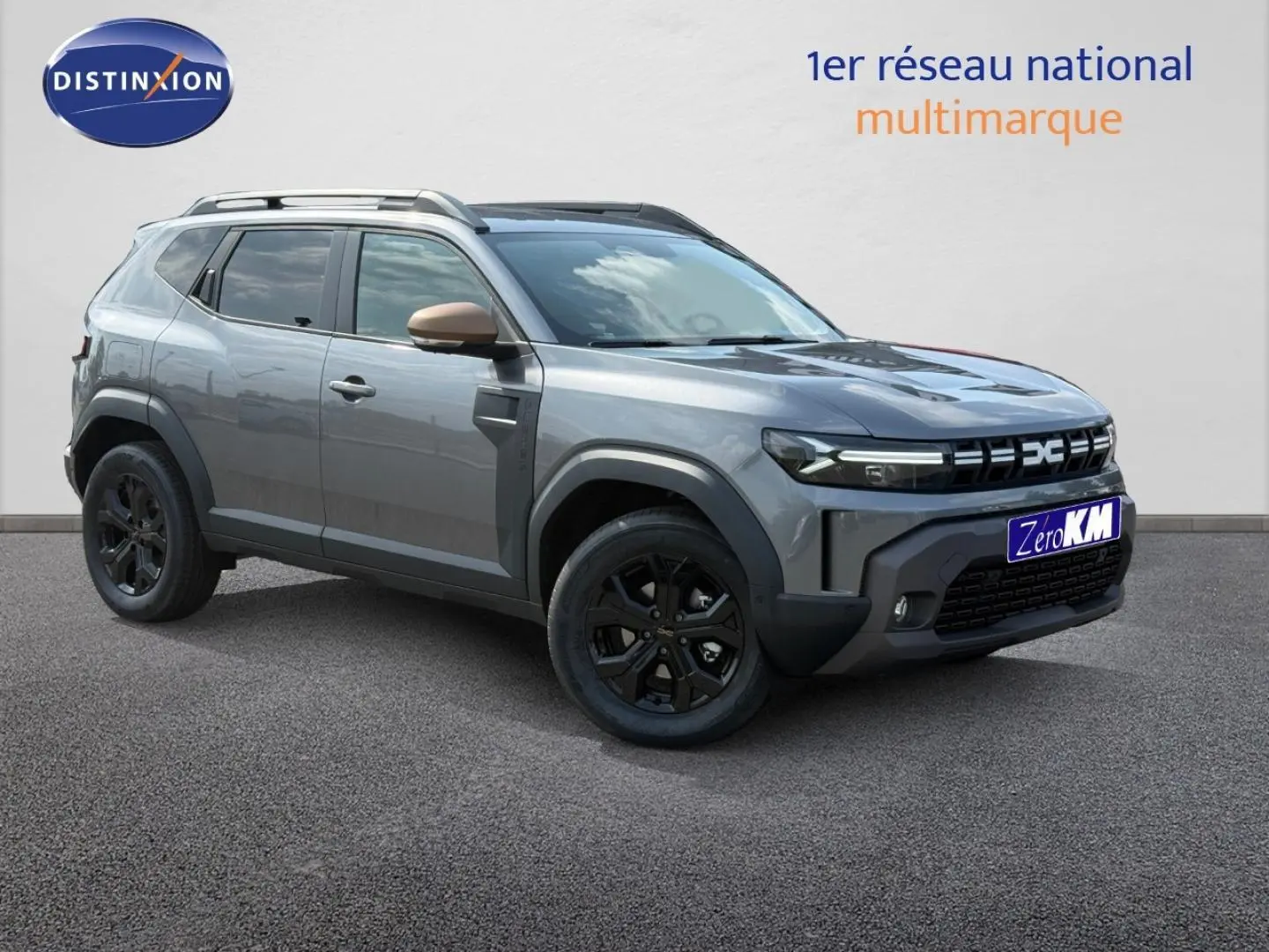 Dacia Duster gris 3/4 avant droit avec jantes noires et rétroviseurs couleur bronze sur fond clair.