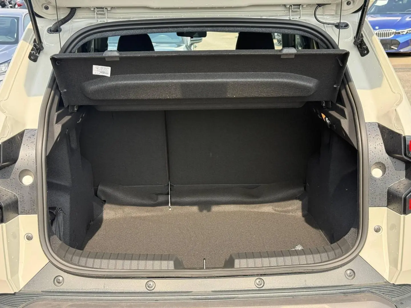 Coffre ouvert vu de l'arrière d'un Dacia Duster gris clair, montrant l'espace de chargement vide et la tablette cache-bagages relevée.