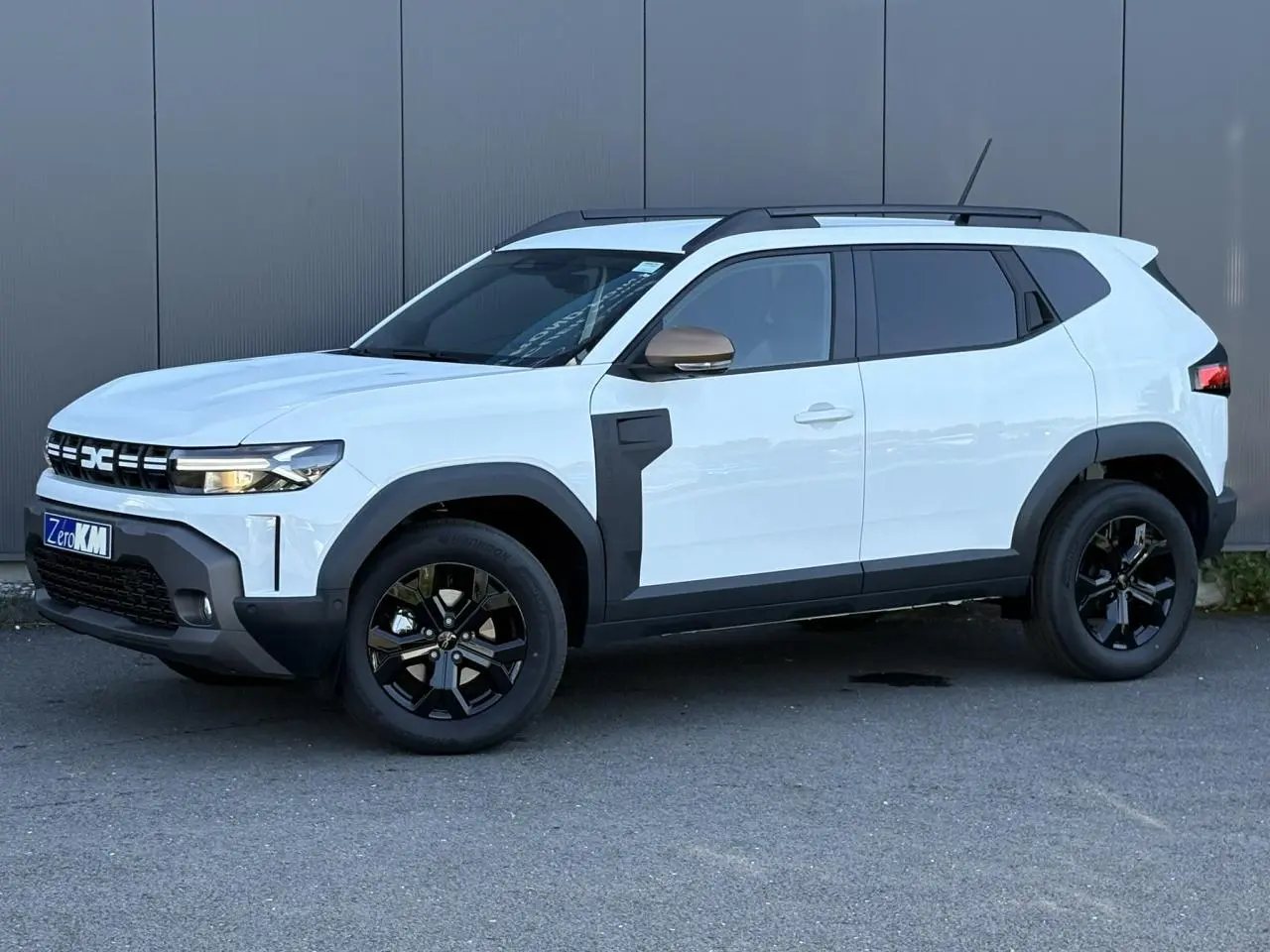 Dacia Duster ECO-G 120 Auto Extrême blanc glacier en vue 3/4 avant droit avec jantes noires et barres de toit.