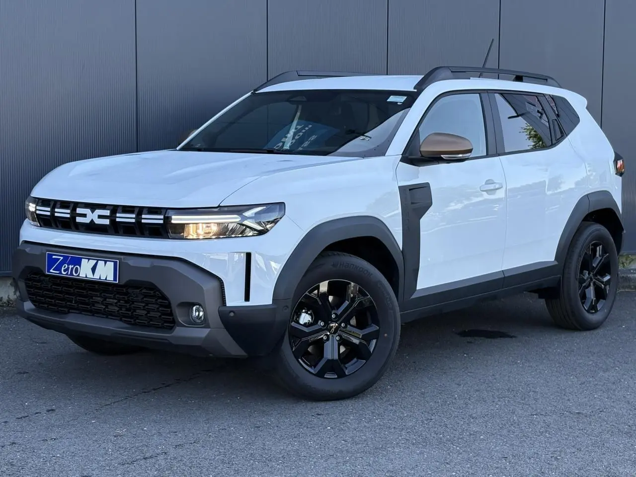 SUV Dacia Duster ECO-G 120 blanc glacier en 3/4 avant droit avec jantes noires et barres de toit noires.