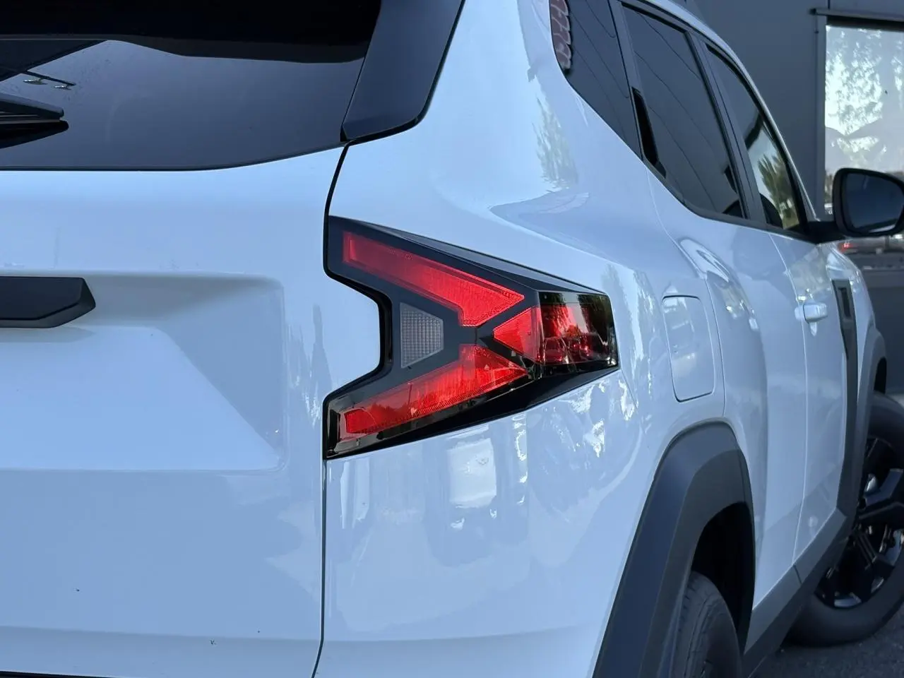 Vue arrière côté gauche du Dacia Duster blanc Glacier 2026 avec feux arrière en forme de flèche et vitres surteintées.