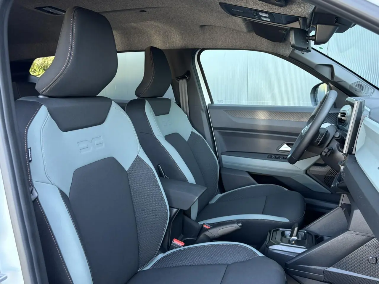 Vue intérieure côté conducteur du Dacia Duster 2026, sièges bicolores noir et gris avec accoudoir central.