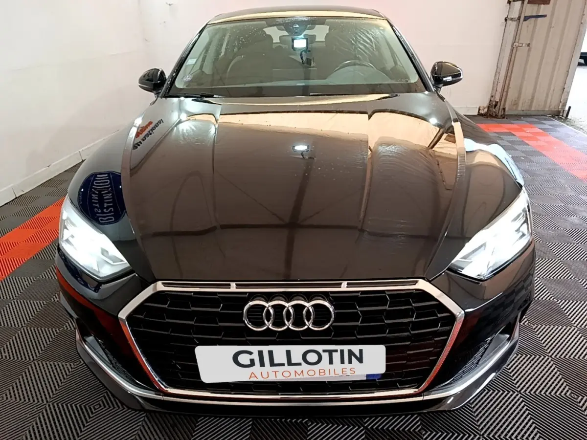 Vue avant d'une Audi A5 noire avec phares LED allumés et calandre hexagonale chromée dans un garage.