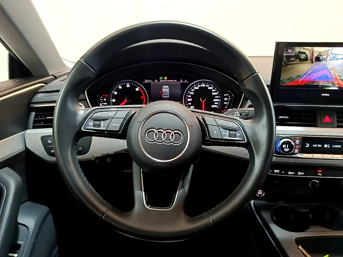 Vue intérieure centrée sur le volant cuir noir d'une Audi A5 35 TFSI 2021 avec tableau de bord digital et écran multimédia.