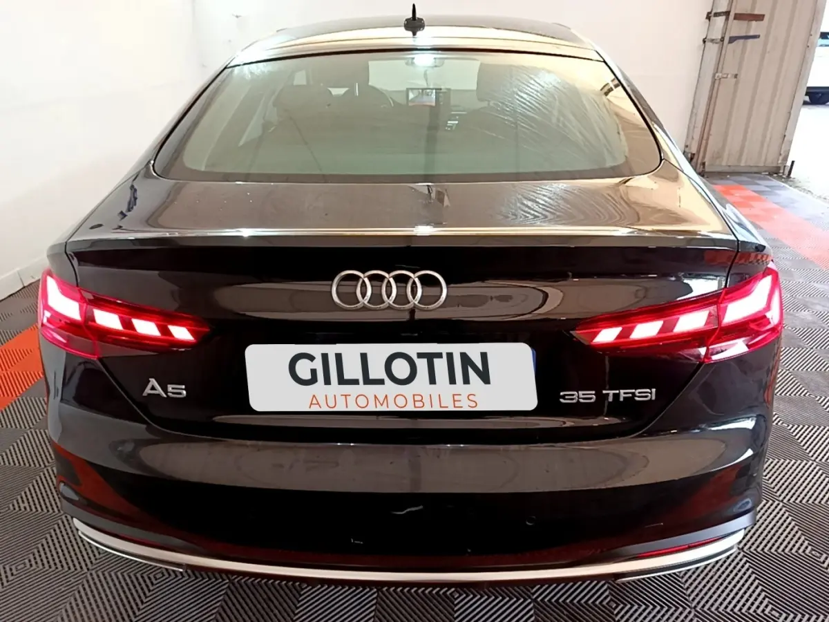 Vue arrière d'une Audi A5 noire 35 TFSI avec feux LED allumés et logo Audi bien visible.