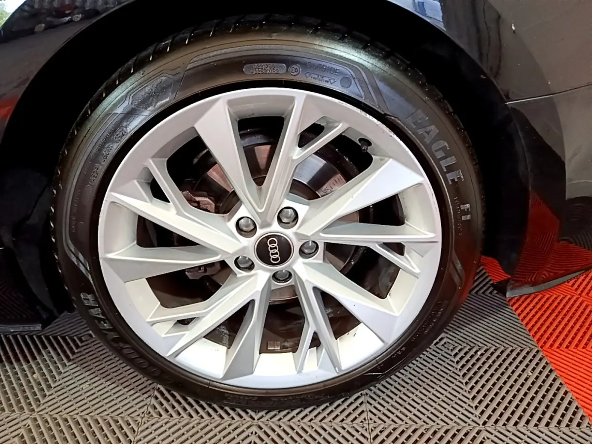 Gros plan sur la jante argentée à dix branches de l'Audi A5 noire, avec pneu Goodyear Eagle visible au sol.