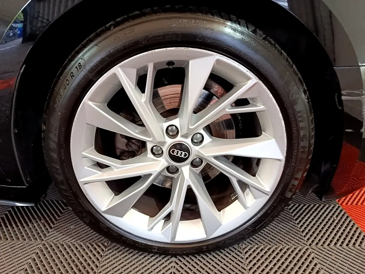 Gros plan sur la roue avant droite d'une Audi A5 noire, mettant en valeur la jante argentée à design étoilé.