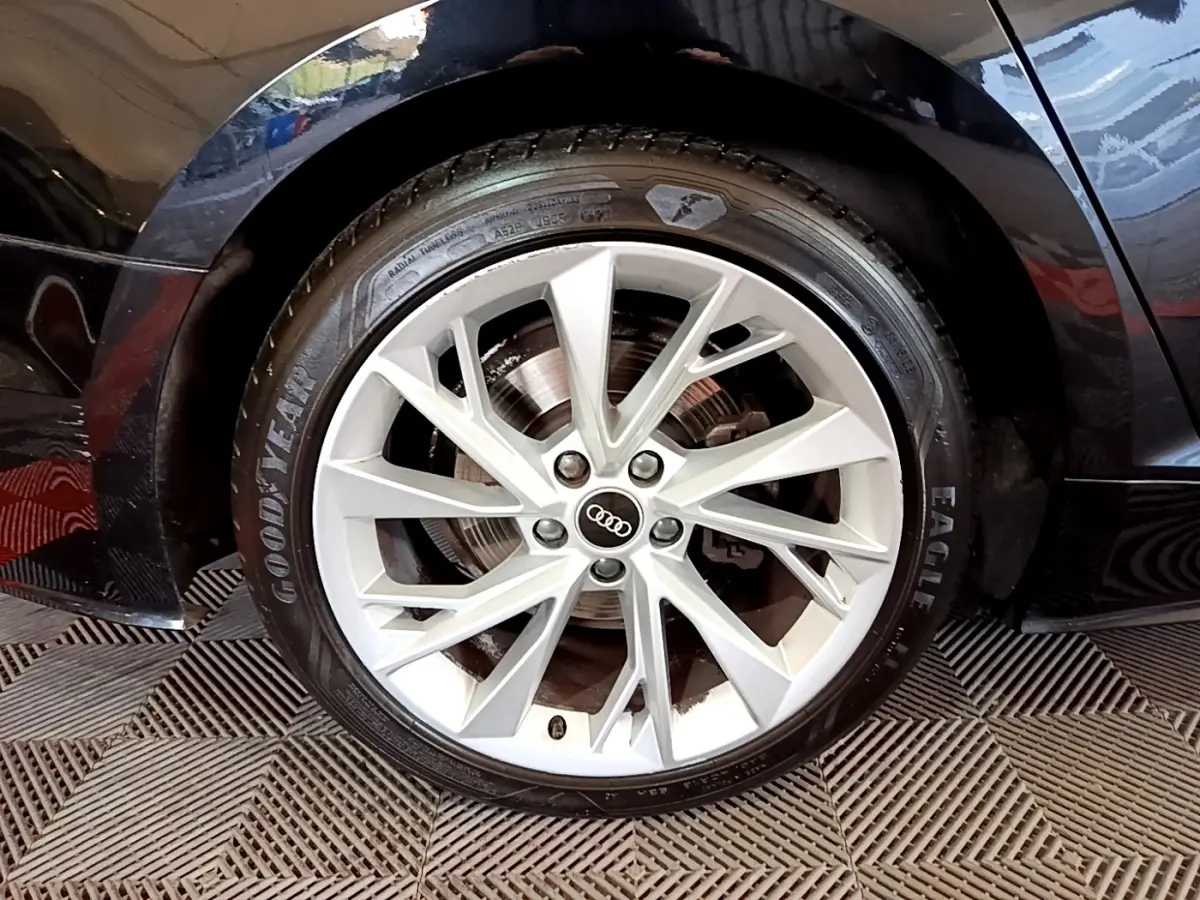 Gros plan sur la roue avant droite noire d'une Audi A5 35 TFSI 150 S TRONIC 7 BUSI LINE avec jante argentée multi-branches.