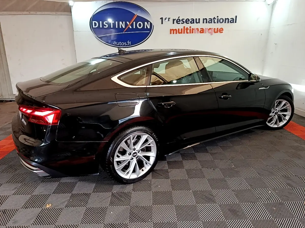 Audi A5 noire vue de 3/4 arrière droit, avec feux LED allumés et jantes argentées dans un showroom.