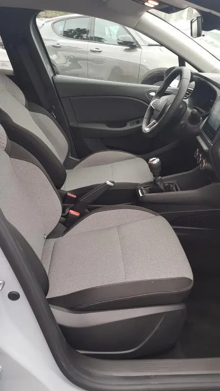 Vue intérieure côté conducteur de la Renault Clio gris 2025, montrant sièges tissu clair et levier de vitesse manuel.