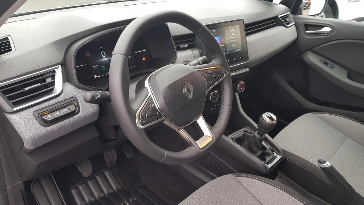 Vue intérieure côté conducteur de la Renault Clio 2025 gris, volant multifonction et boîte manuelle visible.