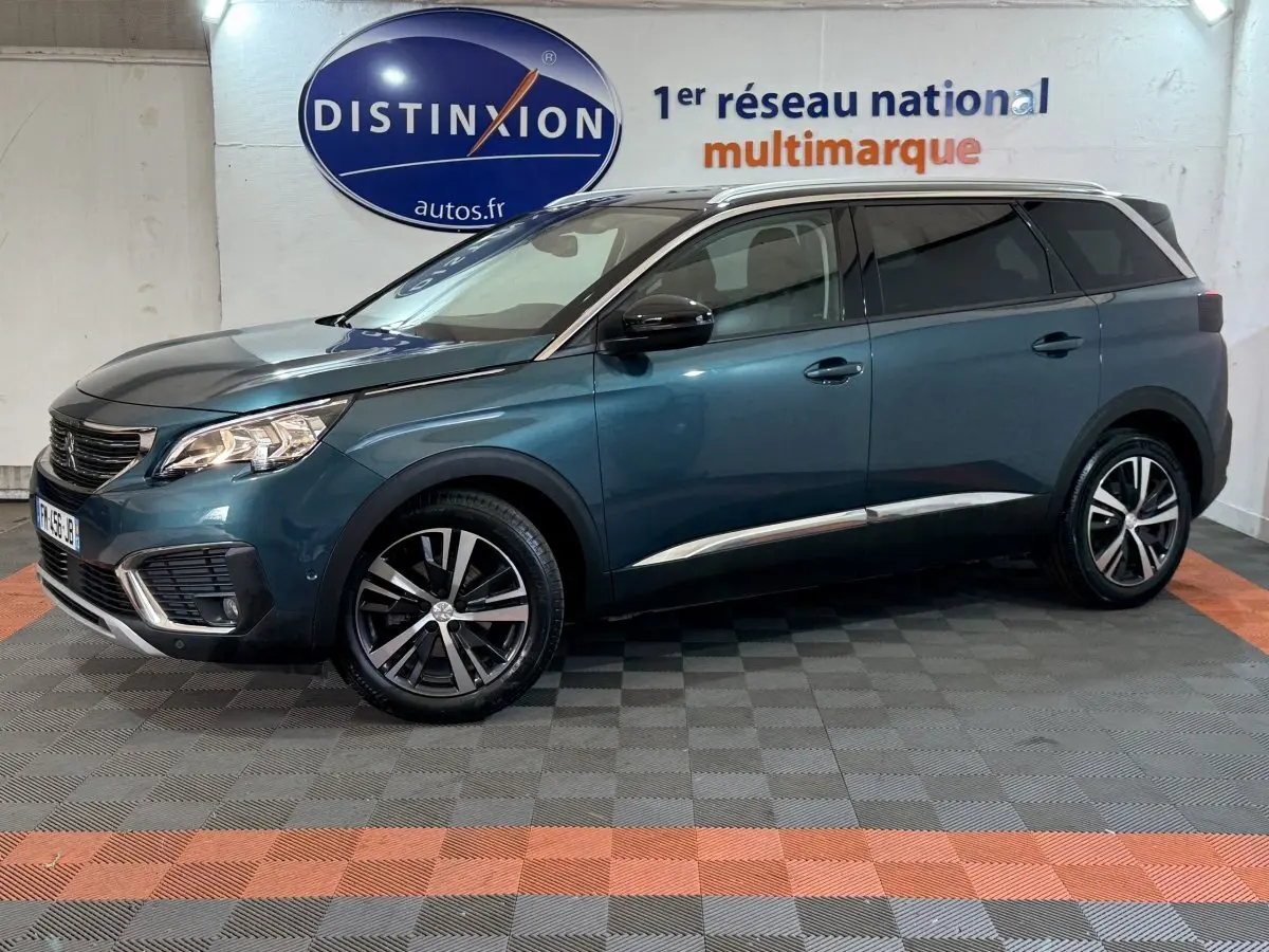 Vue latérale droite d'un Peugeot 5008 bleu métallisé, avec jantes alliage et toit chromé dans un showroom.