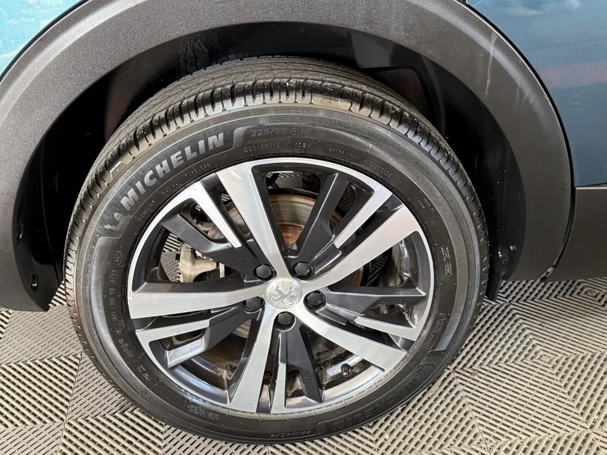 Gros plan sur la roue avant droite d’un Peugeot 5008 bleu, avec jante alliage bicolore et pneu Michelin.