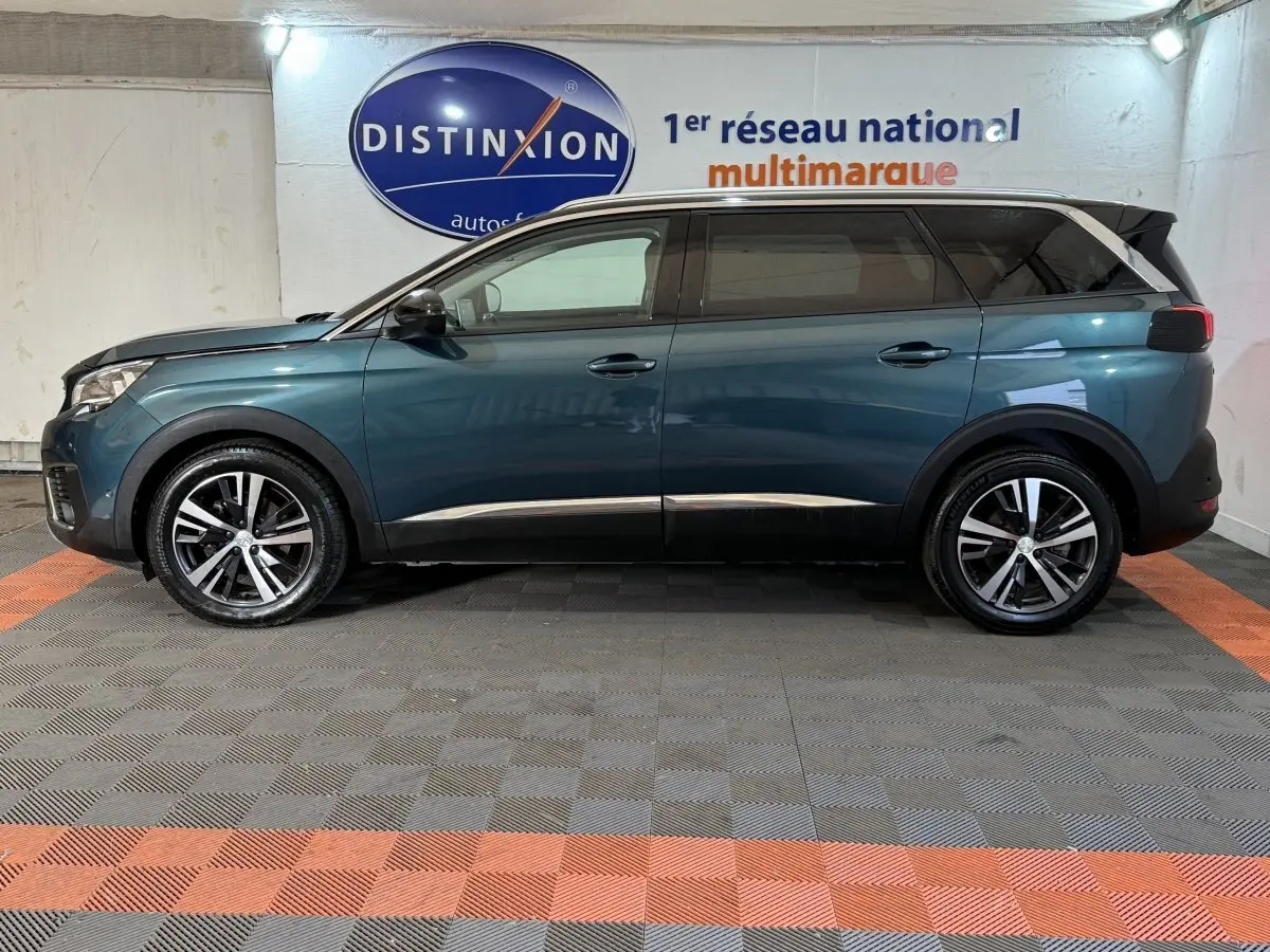 Vue de profil côté gauche d’un Peugeot 5008 bleu avec jantes alliage et vitres teintées dans un showroom intérieur.