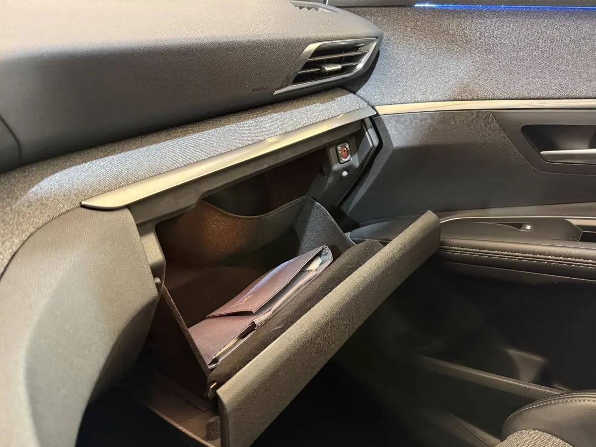 Vue intérieure côté passager du Peugeot 5008 bleu 2019, boîte manuelle, montrant la boîte à gants ouverte avec un document à l'intérieur.