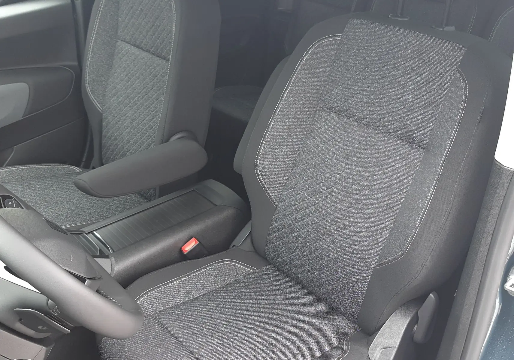 Vue intérieure du Peugeot Rifter 2026 montrant les sièges avant en tissu gris avec accoudoir côté droit, porte ouverte côté conducteur.