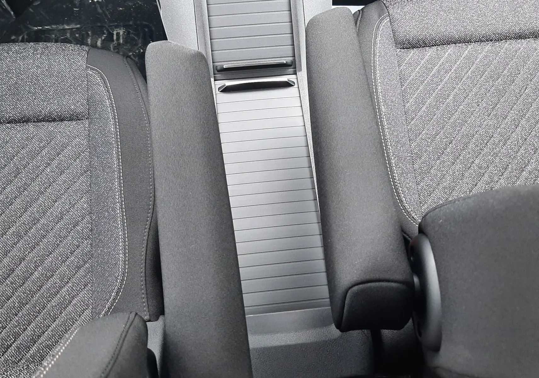 Vue intérieure rapprochée du Peugeot Rifter 2026 montrant la console centrale et les accoudoirs en tissu gris.
