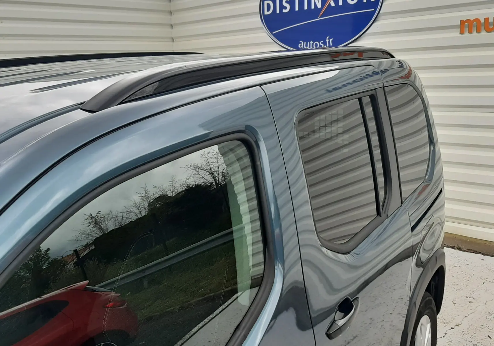 Vue latérale droite du Peugeot Rifter bleu Kiama 2026, mettant en valeur les vitres teintées et la barre de toit noire.