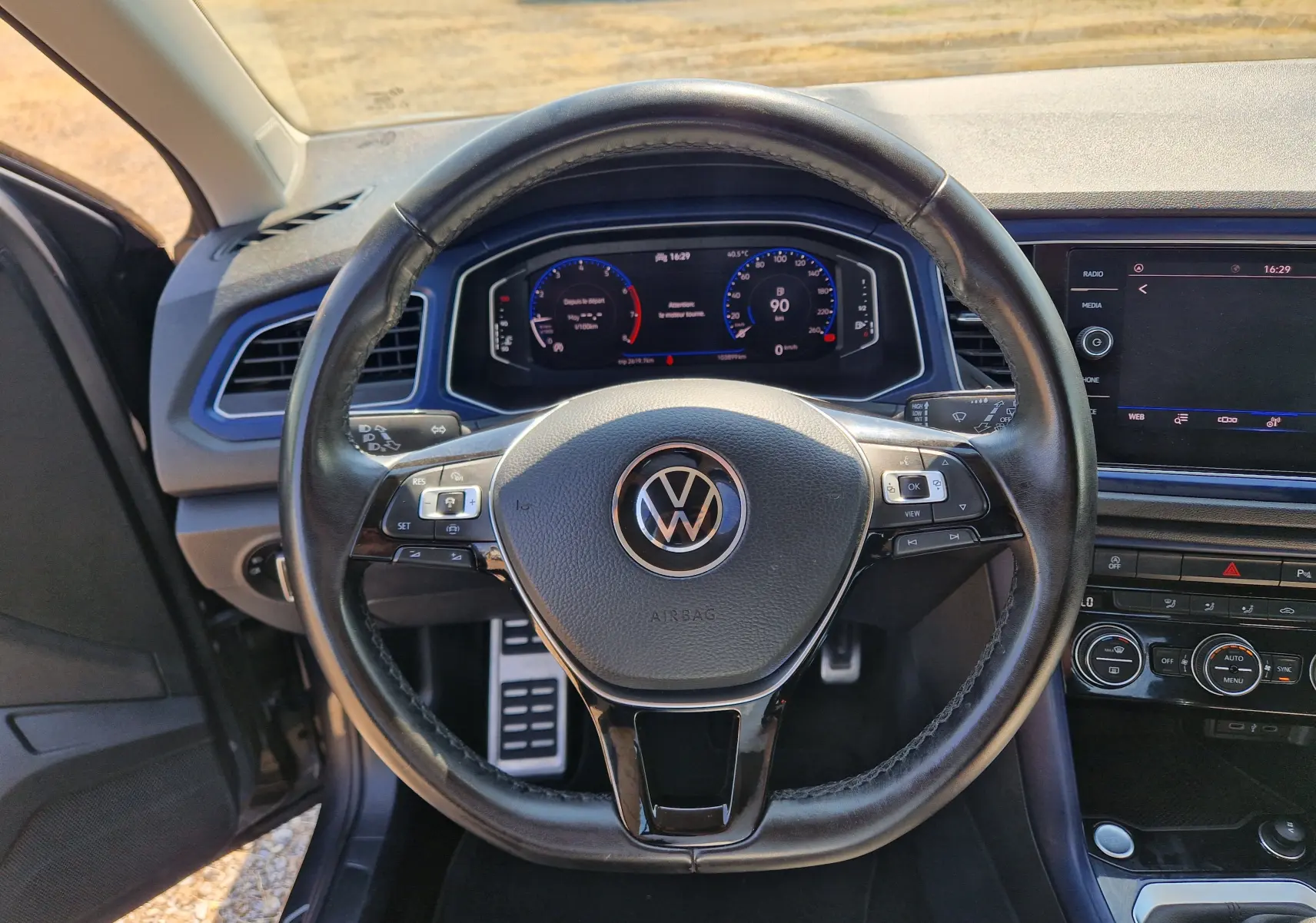 Vue intérieure centrée sur le volant noir du Volkswagen T-Roc 1.0 TSI 115 UNITED avec tableau de bord numérique et écran tactile.