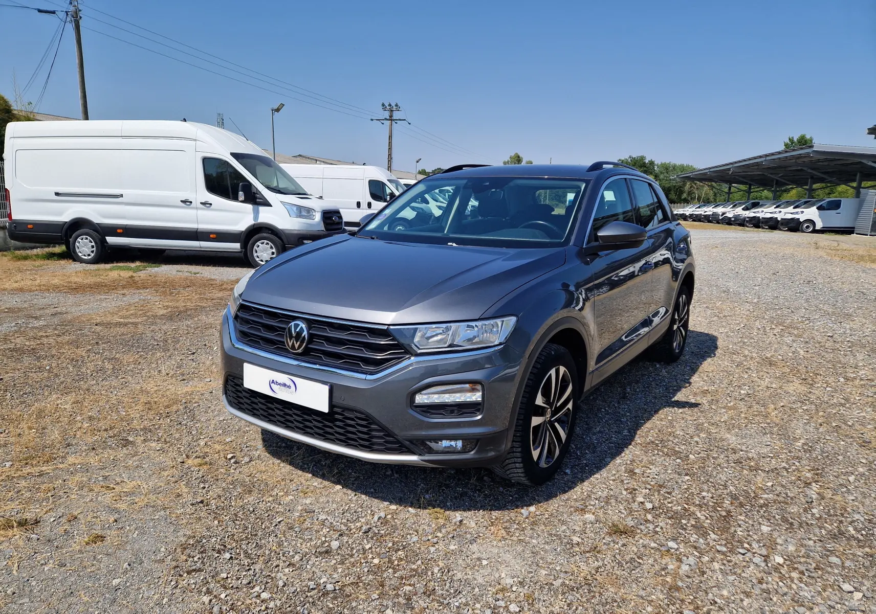 Volkswagen T-Roc gris foncé métal en 3/4 avant droit, avec jantes alliage et calandre noire distinctive.