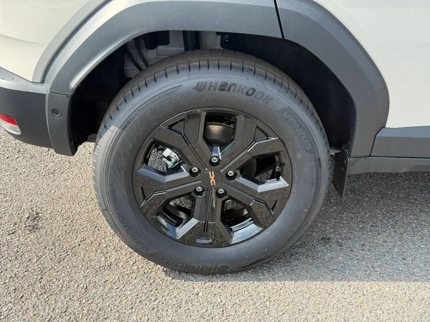 Gros plan sur la roue arrière droite du Dacia Duster blanc 2026 avec jante alu noire et logo central orange.