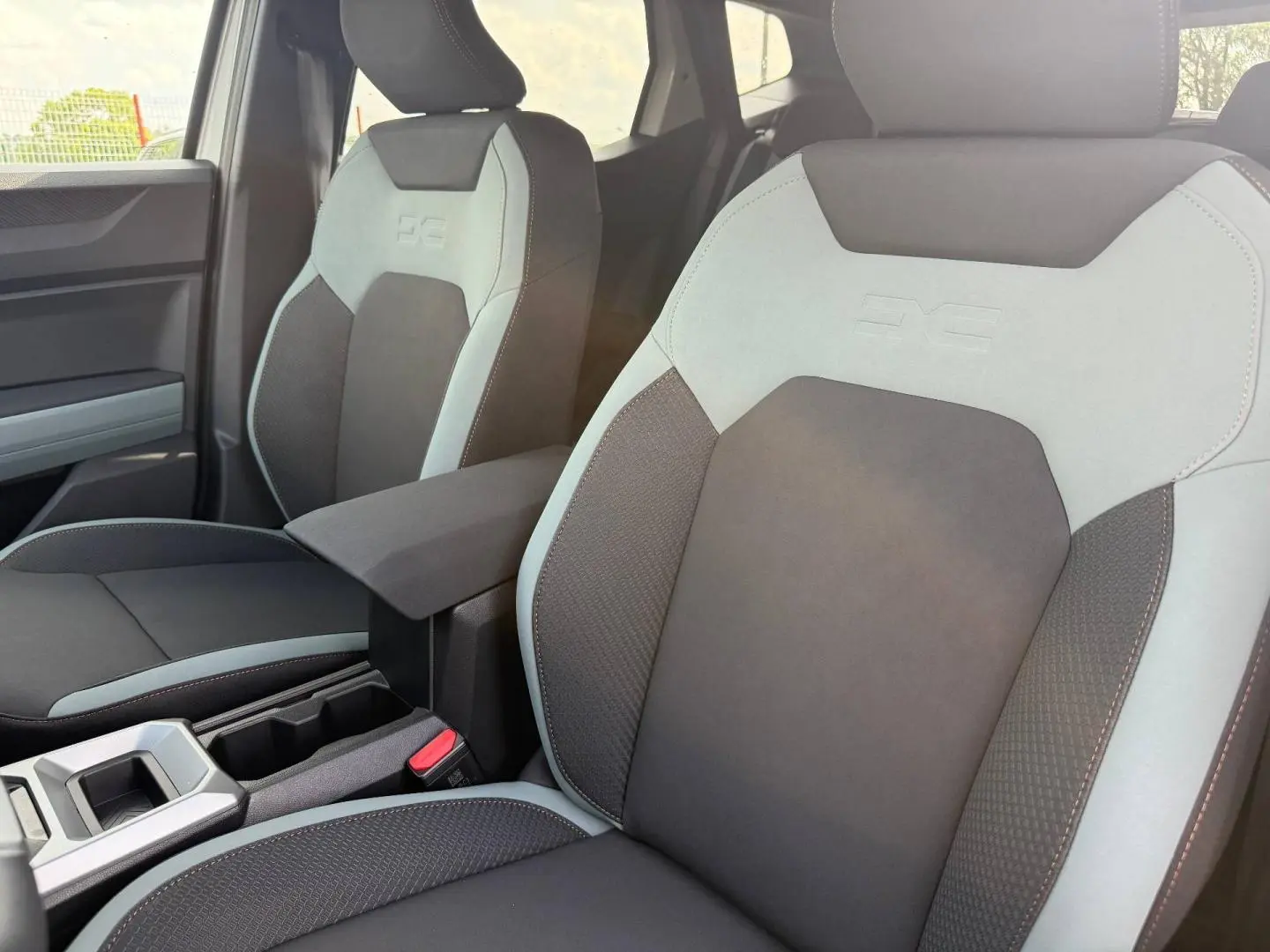Vue rapprochée des sièges avant gris et noirs du Dacia Duster 2026 avec accoudoir central et logo DC embossé.
