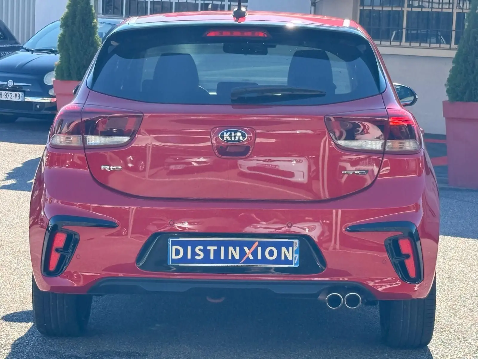 Vue arrière d'une KIA RIO rouge grenadine 2022 avec double sortie d'échappement et plaque Distinxion visible.