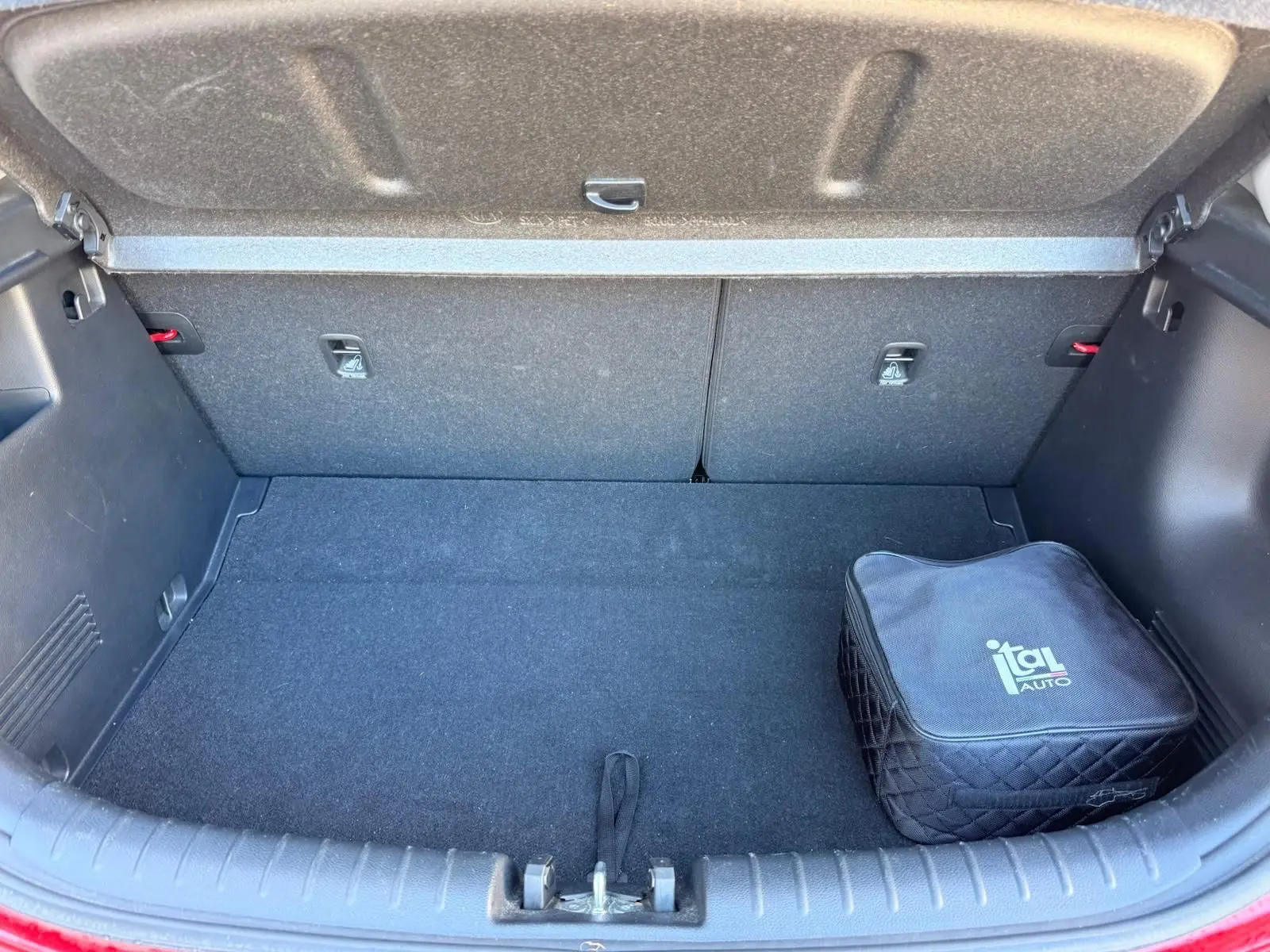 Coffre ouvert d'une KIA RIO rouge grenadine 2022, montrant un espace de rangement propre avec une trousse noire Ital Auto.
