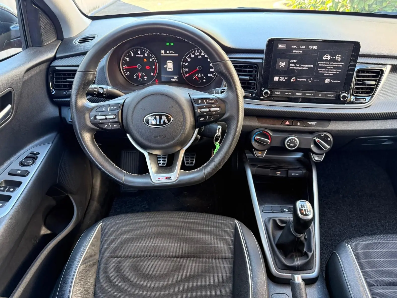 Vue intérieure du poste de conduite de la Kia Rio 2022, volant multifonction et levier de vitesse manuel visibles.