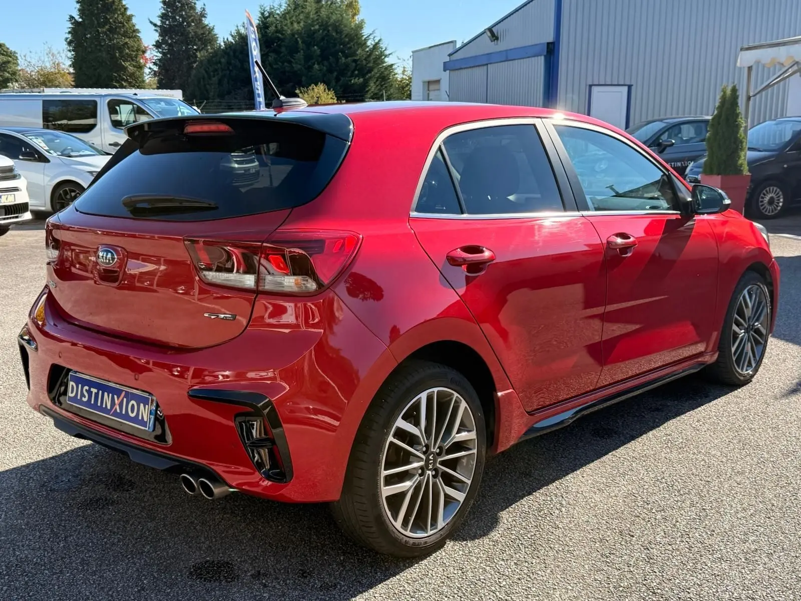 KIA Rio GT-Line rouge grenadine vue 3/4 arrière droit, jantes alliage et double sortie d’échappement visibles.