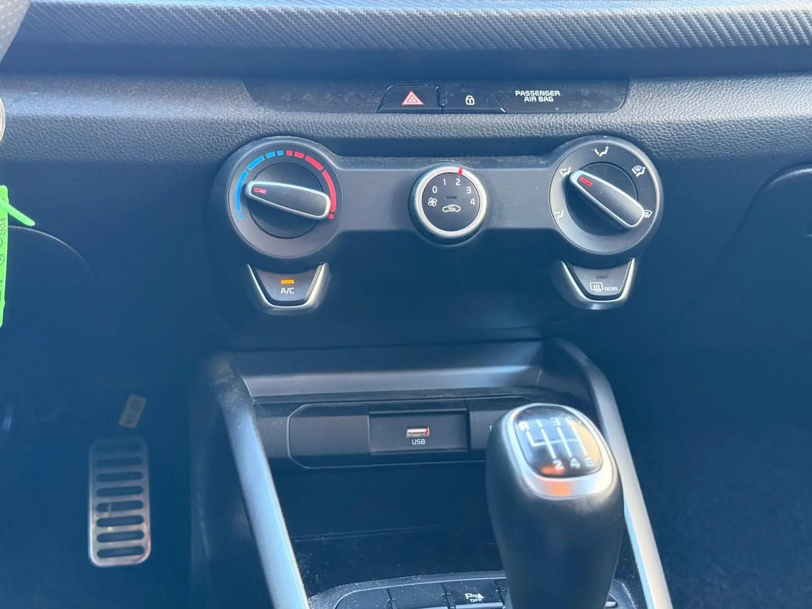 Gros plan sur la console centrale de la KIA RIO rouge grenadine 2022, avec commandes clim et levier de vitesse manuel.