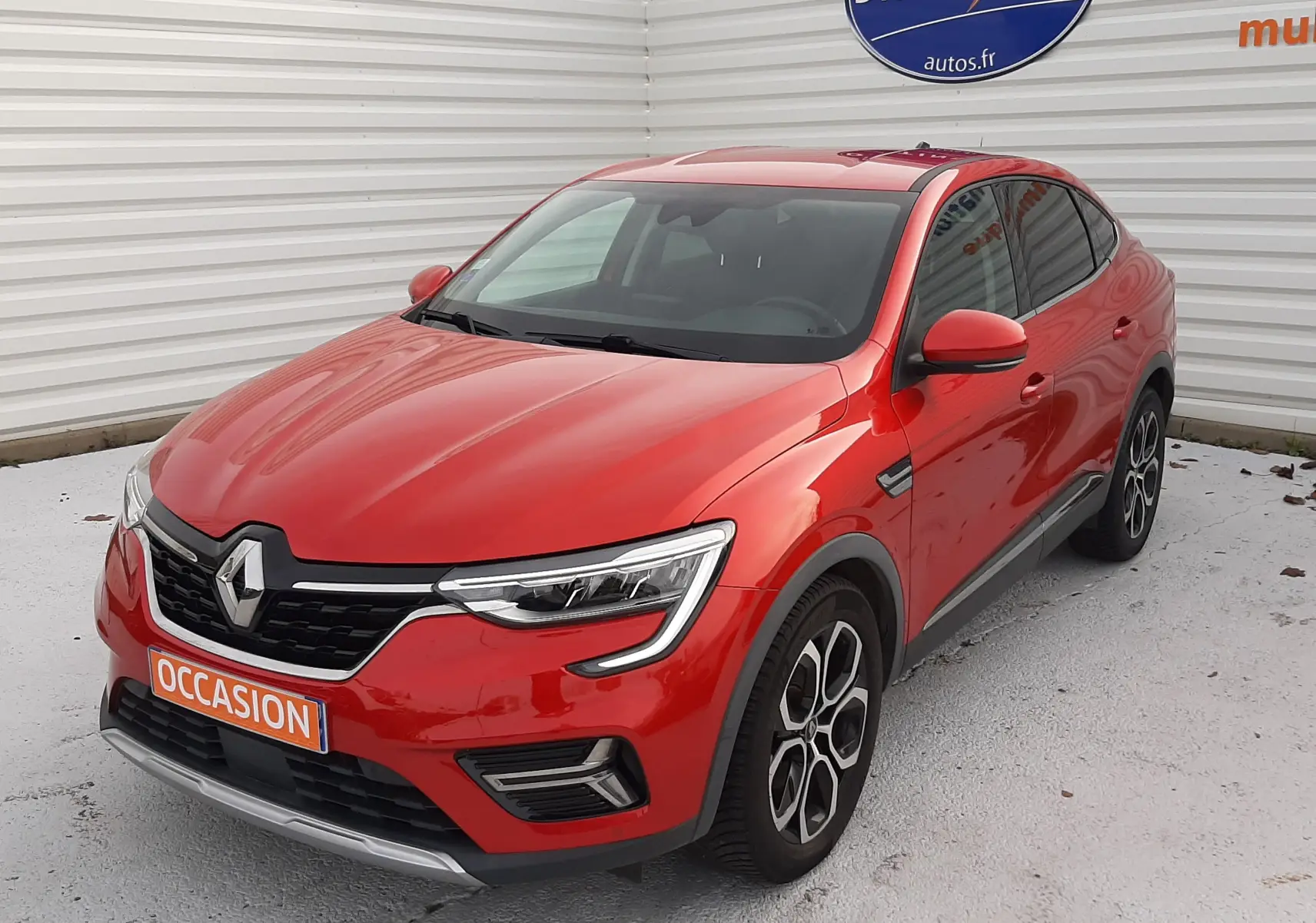 Renault Arkana 1.6 E-TECH rouge Flame en 3/4 avant droit, avec jantes bi-ton et calandre noire distinctive.