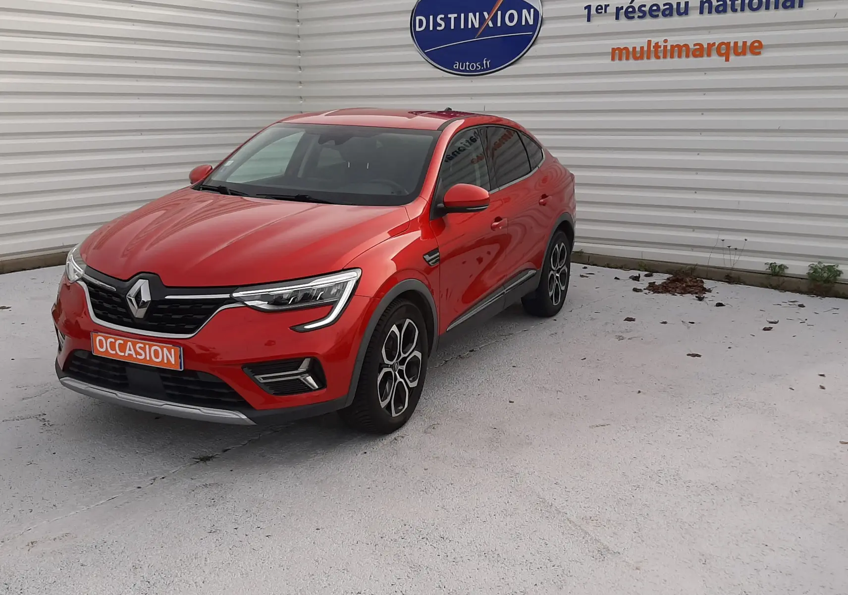 Renault Arkana 1.6 E-TECH rouge Flame en 3/4 avant droit, avec jantes bi-ton et calandre noire distinctive.