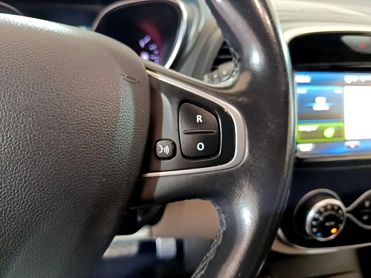 Gros plan sur le volant cuir noir avec commandes vocales du Renault Captur Intens TCe 150 de 2019, tableau de bord flou en arrière-plan.