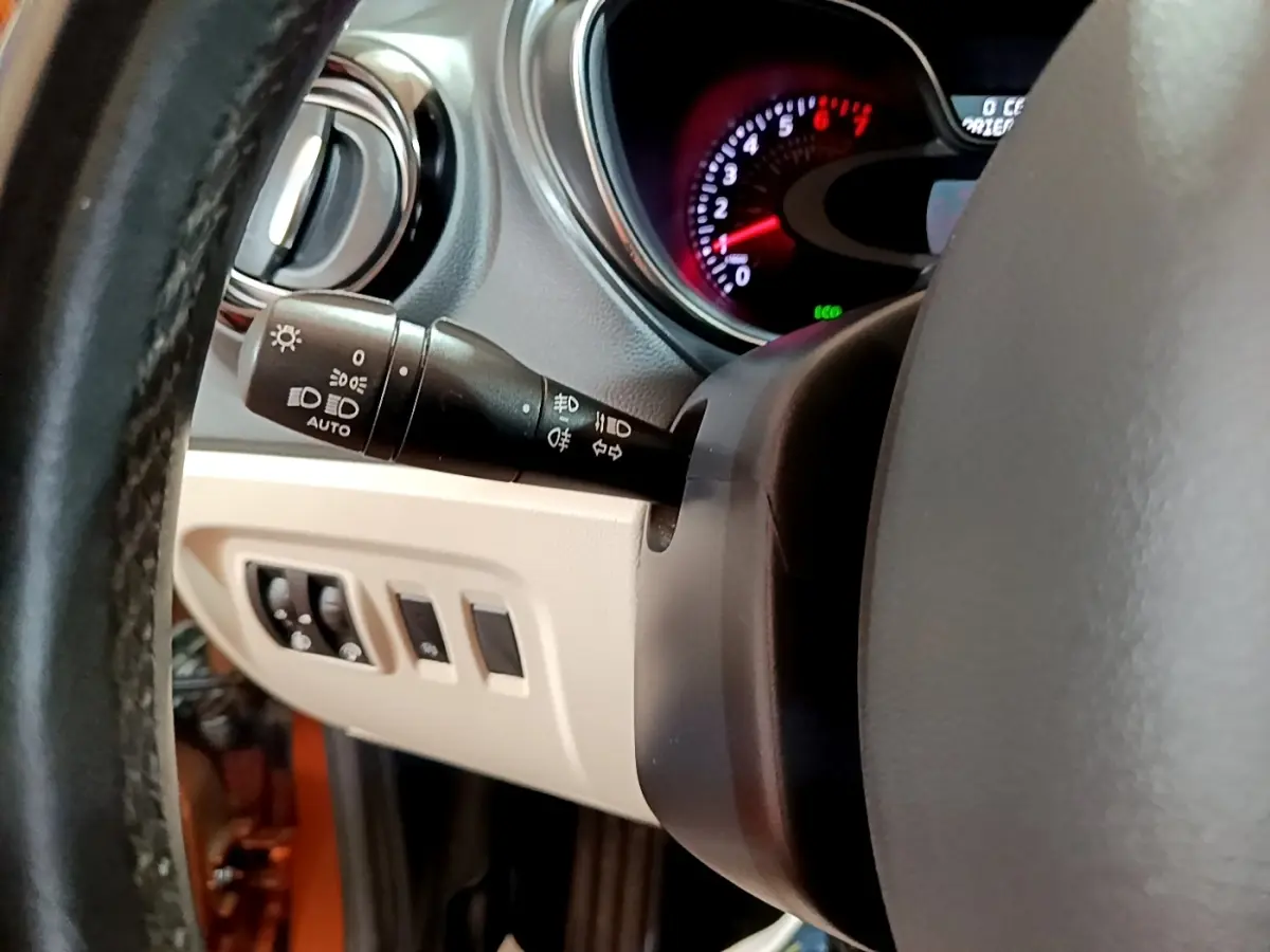 Gros plan sur la commande des phares et le tableau de bord du Renault Captur Intens orange, côté gauche du volant.