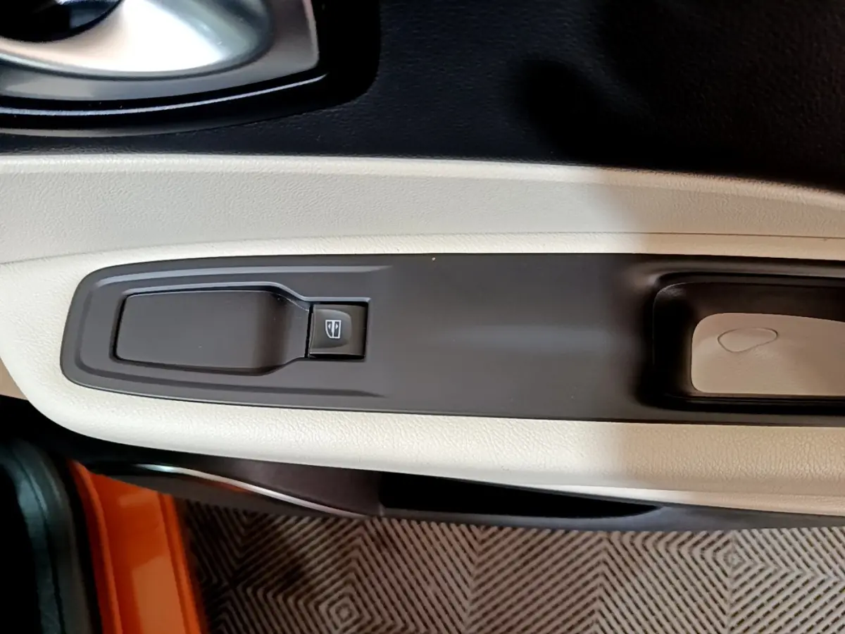 Gros plan sur la commande de lève-vitre côté conducteur du Renault Captur orange, avec garniture beige et noire.