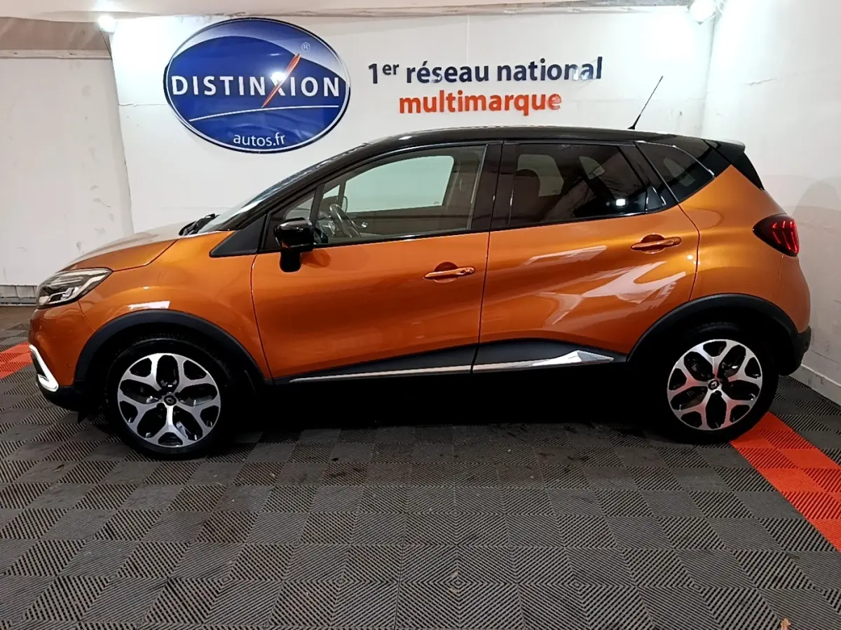 Profil côté gauche d'un Renault Captur Intens orange 2019 avec toit noir dans un showroom Distinxion.