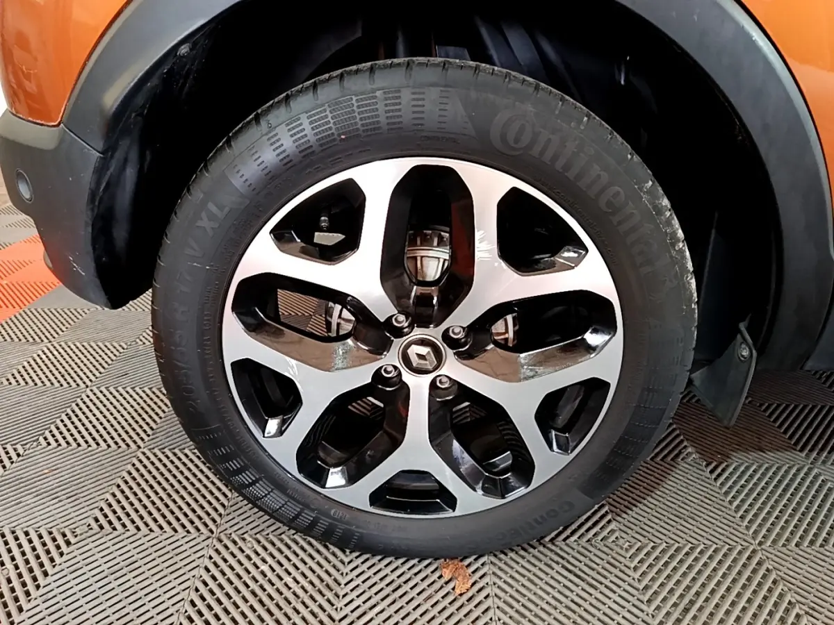 Gros plan sur la roue avant gauche du Renault Captur orange, mettant en valeur la jante alliage bicolore et le logo Renault central.