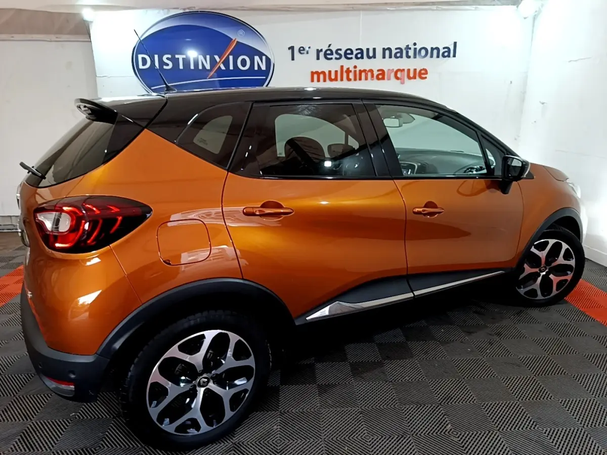 Profil droit du Renault Captur Intens orange 2019 avec toit noir et jantes alliage distinctives dans un showroom.
