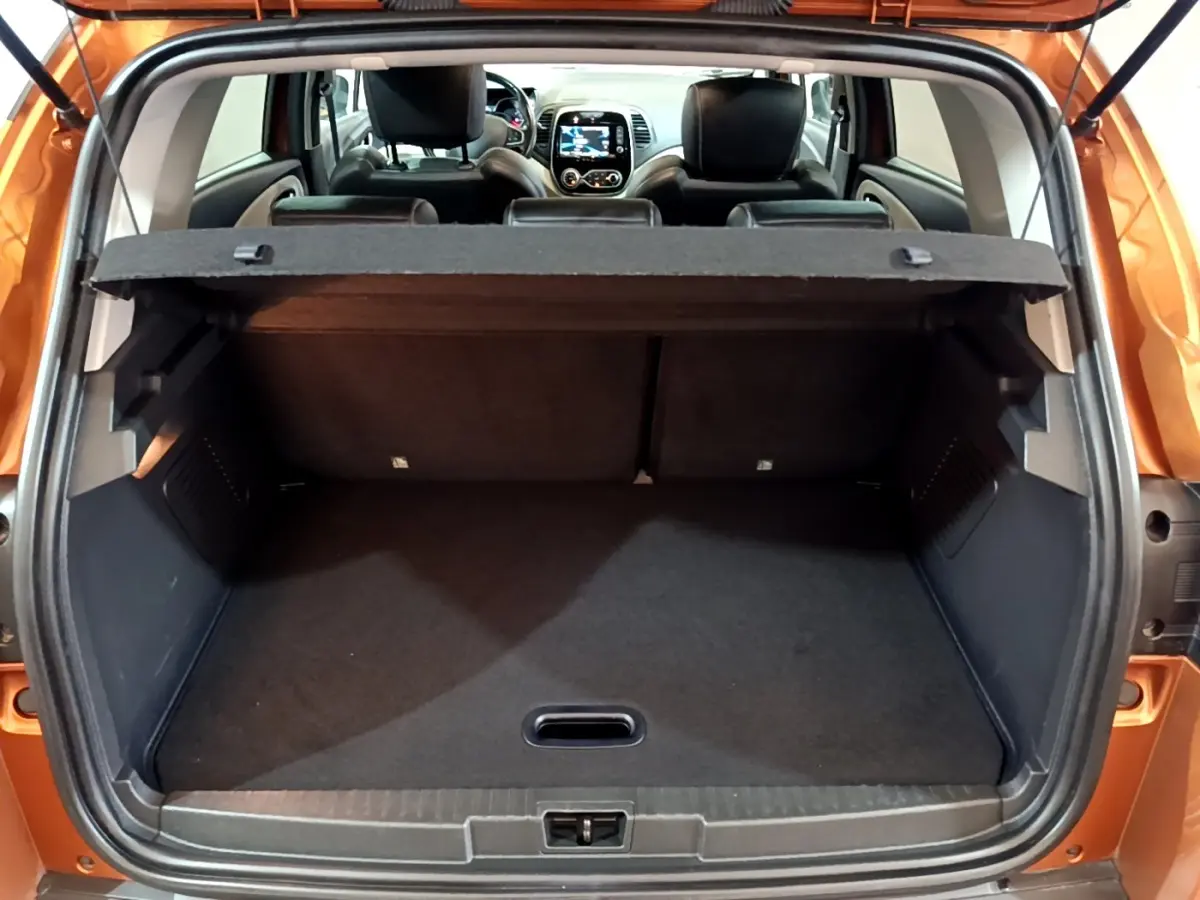 Coffre ouvert vu de l'arrière d'un Renault Captur orange 2019 avec tablette cache-bagages et sièges arrière noirs visibles.