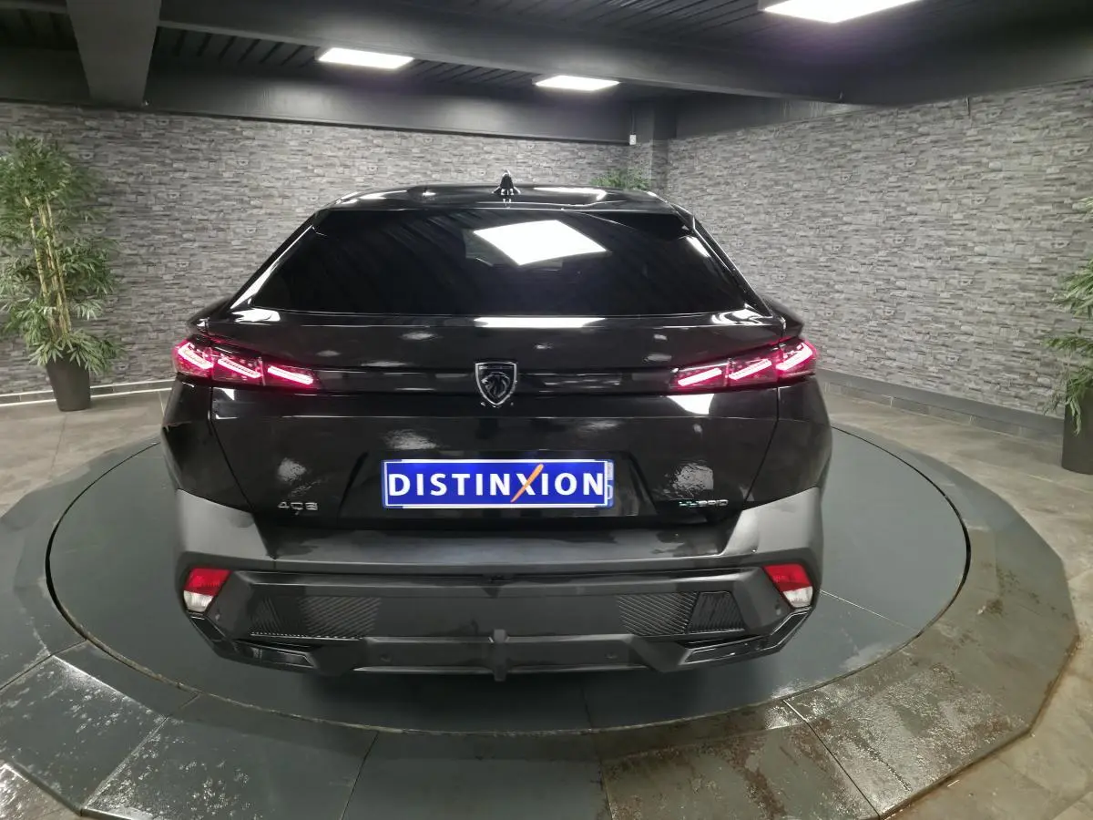 Vue arrière d'une Peugeot 408 noire avec feux arrière LED allumés dans un showroom intérieur.