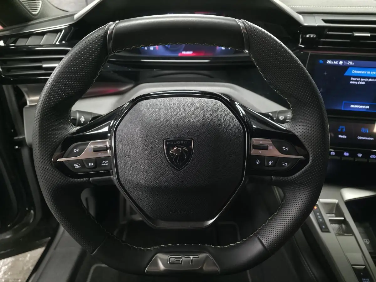 Volant cuir perforé noir avec badge GT au centre, tableau de bord numérique et écran tactile du Peugeot 408 1.6 PHEV 2024.