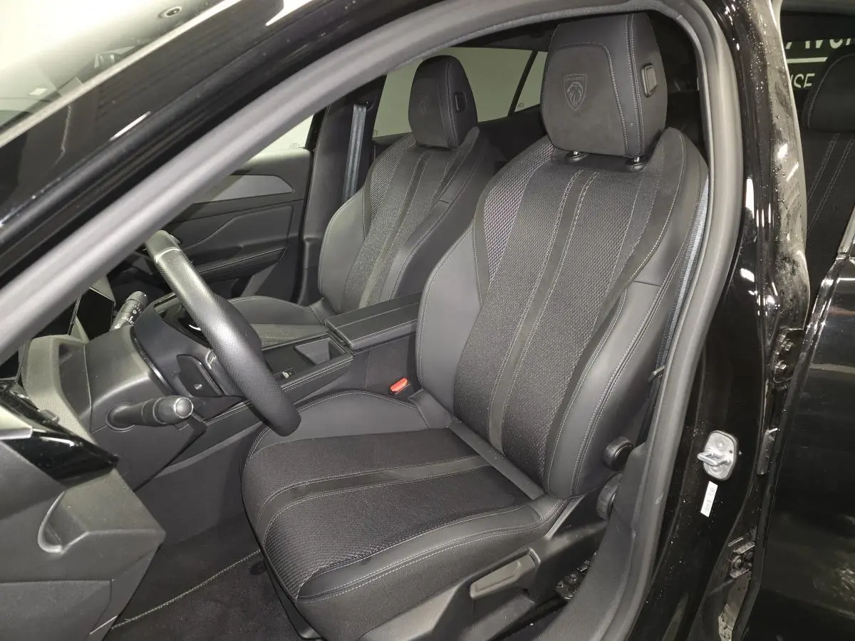 Vue intérieure côté conducteur de la Peugeot 408 noire 2024, sièges sport en tissu et cuir avec logo Peugeot brodé.