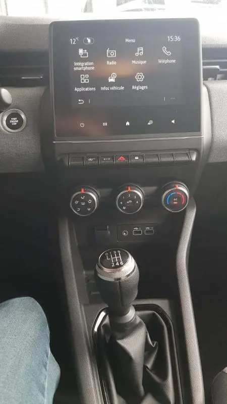 Vue intérieure centrée sur la console centrale d'une Renault Clio gris 2025, avec écran tactile et levier de vitesses manuel.