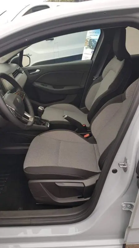 Intérieur avant droit d'une Renault Clio gris 2025, sièges tissu bicolore et boîte manuelle visible.