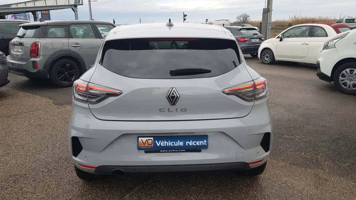 Vue arrière d'une Renault Clio gris clair 2025 avec feux allumés et vitres surteintées en extérieur.