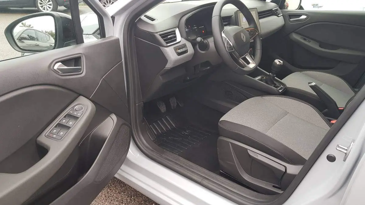Vue intérieure côté conducteur de la Renault Clio gris 2025, montrant le volant, la boîte manuelle et les commandes de porte.