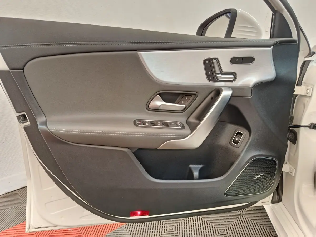Vue intérieure de la porte avant gauche blanche d'une Mercedes Classe A 250 e AMG Line avec garniture cuir et insert alu.
