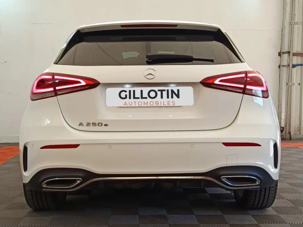 Vue arrière d'une Mercedes Classe A 250 e AMG Line blanche, avec feux LED allumés et double sortie d'échappement chromée.